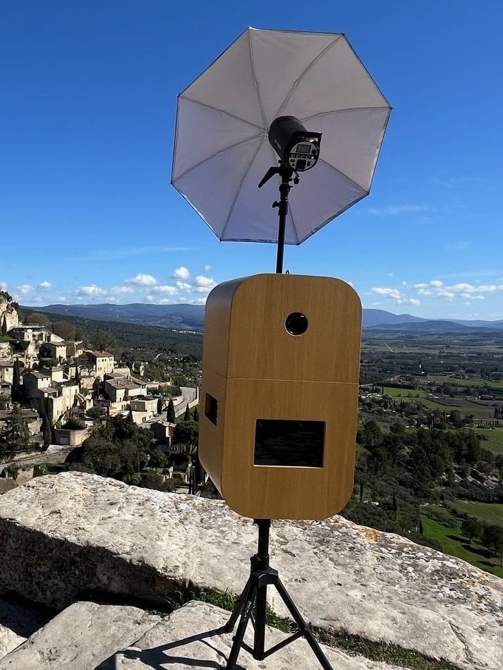 La borne photobooth Provence Photobooth avec son flash parapluie, devant un village perché du Luberon